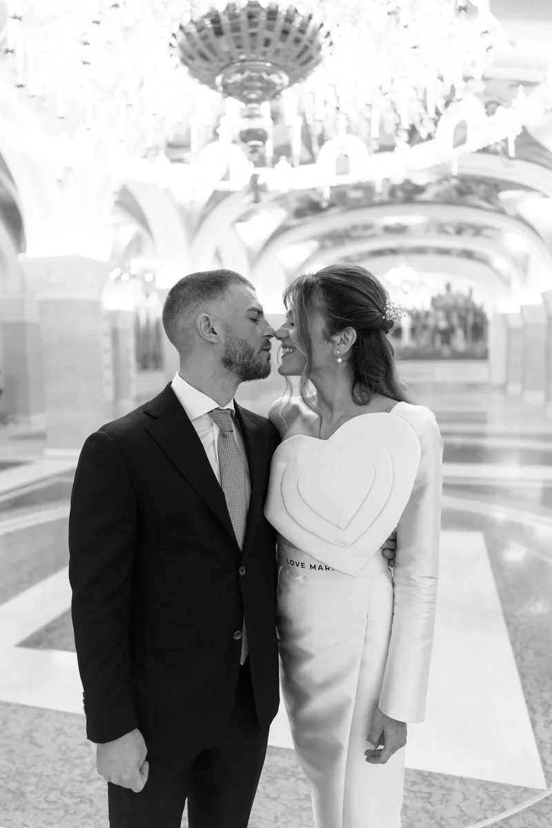 Bride and groom lean in for a kiss beneath a glittering crystal chandelier.