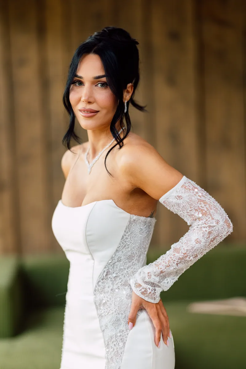 Bride in a fitted white mermaid gown with lace panel and glove poses with a hand on her hip