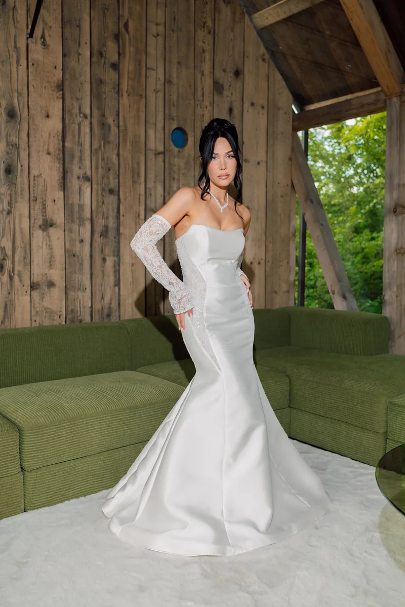 Full length bride in a white satin mermaid dress standing in a wooden cabin with green sofas