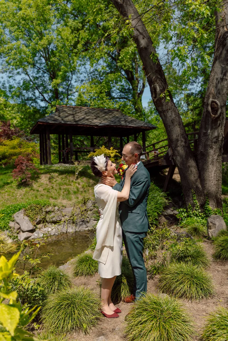 Couple embracing in a green spring garden with a wooden gazebo and pond behind them