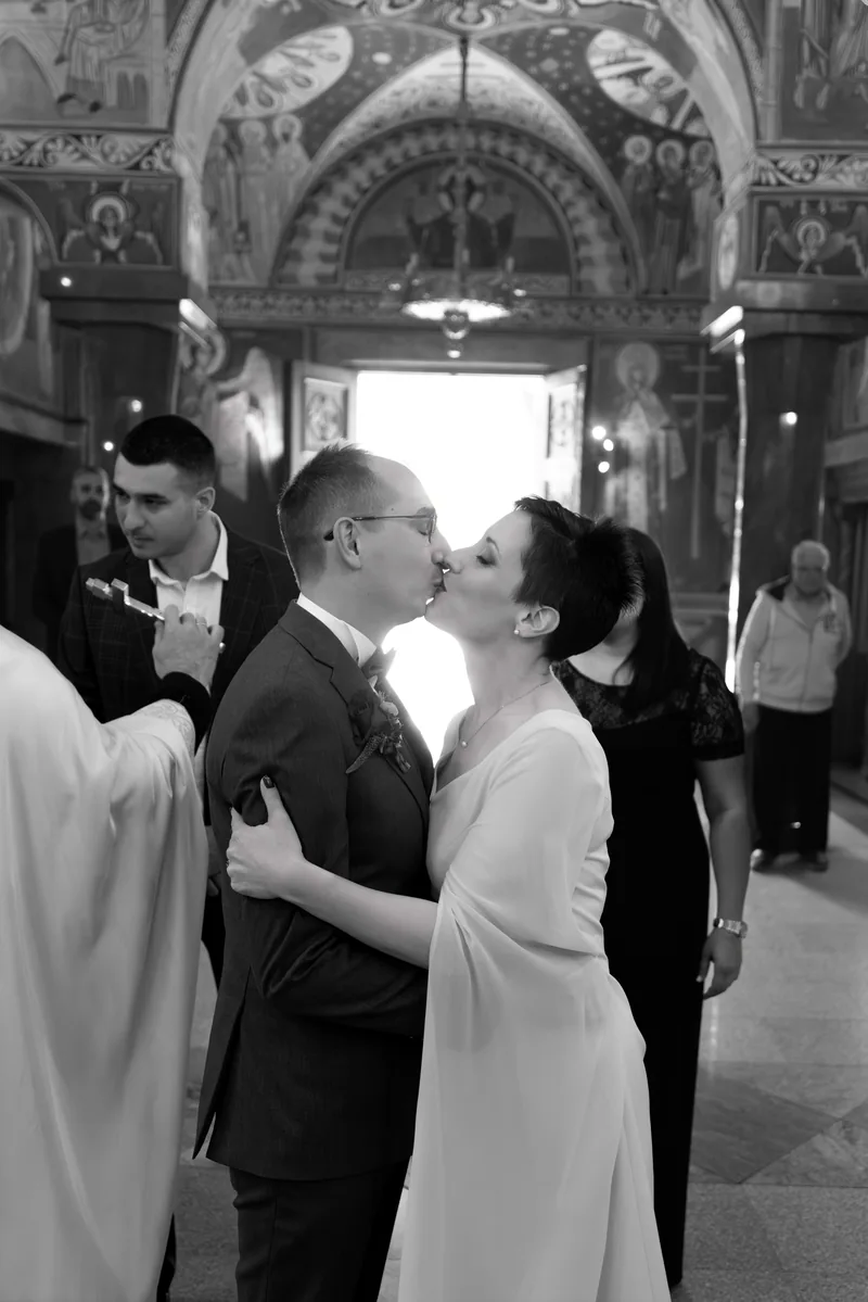 Black and white backlit kiss between a bride and groom in an ornate church doorway with guests
