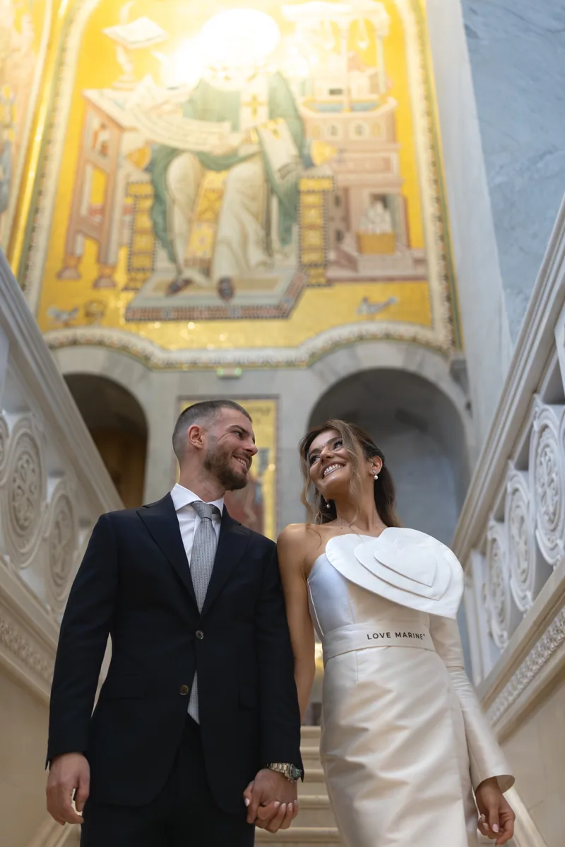 Bride and groom gaze at each other on the stairs below a shimmering golden mosaic.