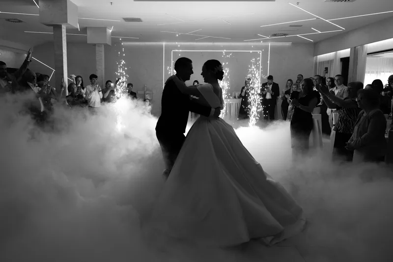 In black and white, a couple dance in silhouette through thick low fog and sparklers surrounded by guests.