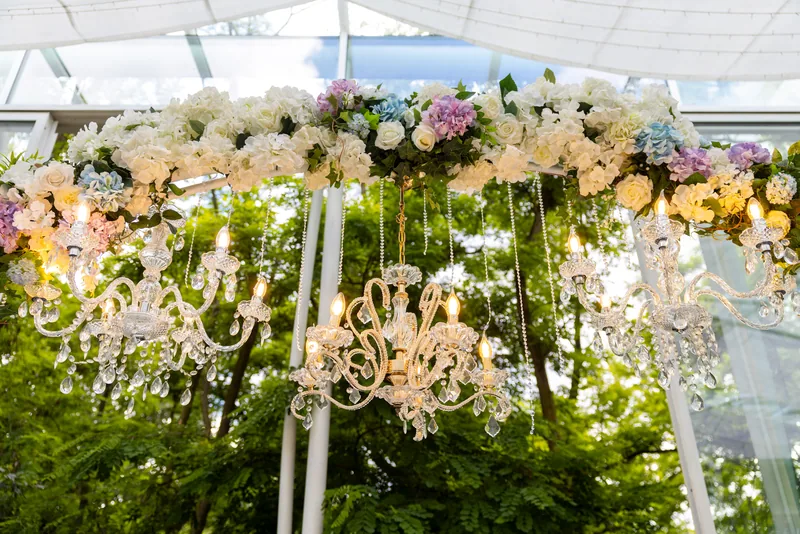 Crystal chandeliers hanging beneath a floral canopy of white, lilac and blue blooms