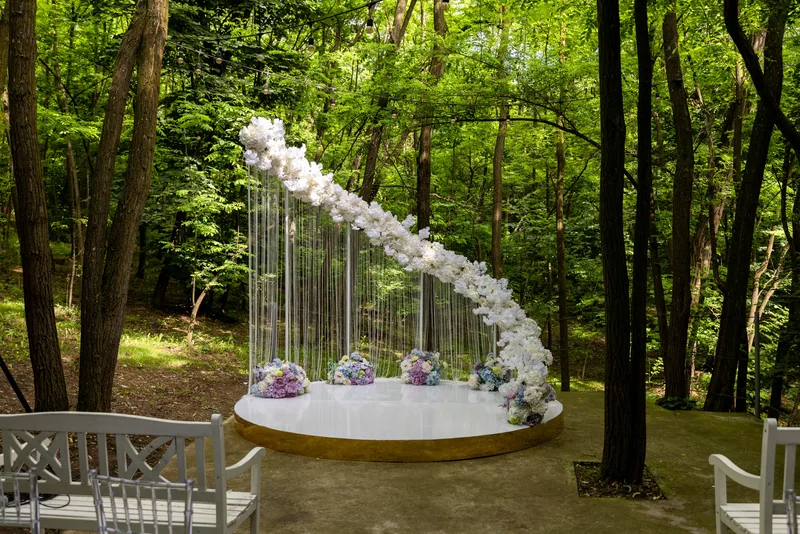 Forest ceremony stage with an arch of cascading white orchids and pastel hydrangeas among trees