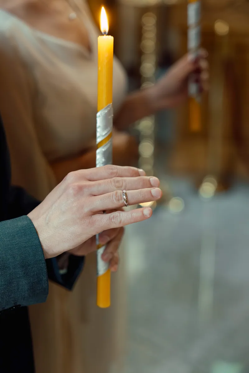 Close-up of hands holding a tall beeswax ceremony candle with a wedding band on the finger