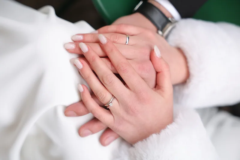 A close view of the couple's hands resting together, showing wedding rings, beside a soft white fur cuff.