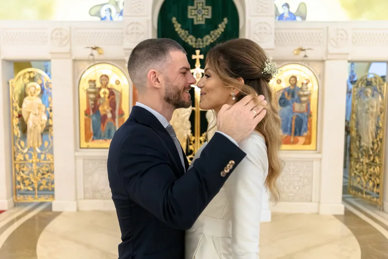 Bride and groom share a tender moment before an ornate iconostasis of saints and gold.