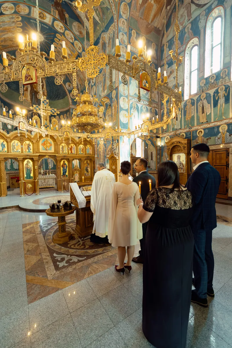 Wedding party and priest stand before a gold iconostasis in a blue frescoed Orthodox church
