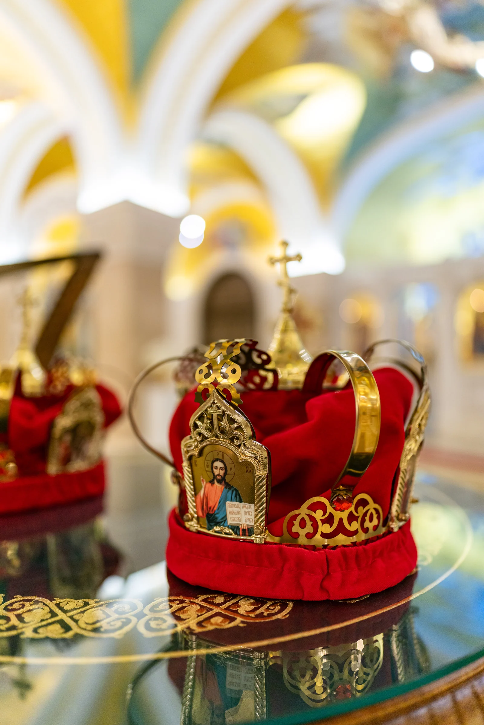 Two Orthodox wedding crowns rest on red velvet beside a small icon of Christ.