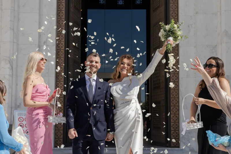 Newlyweds cheer as the bridal party showers them with white petals outside the church.