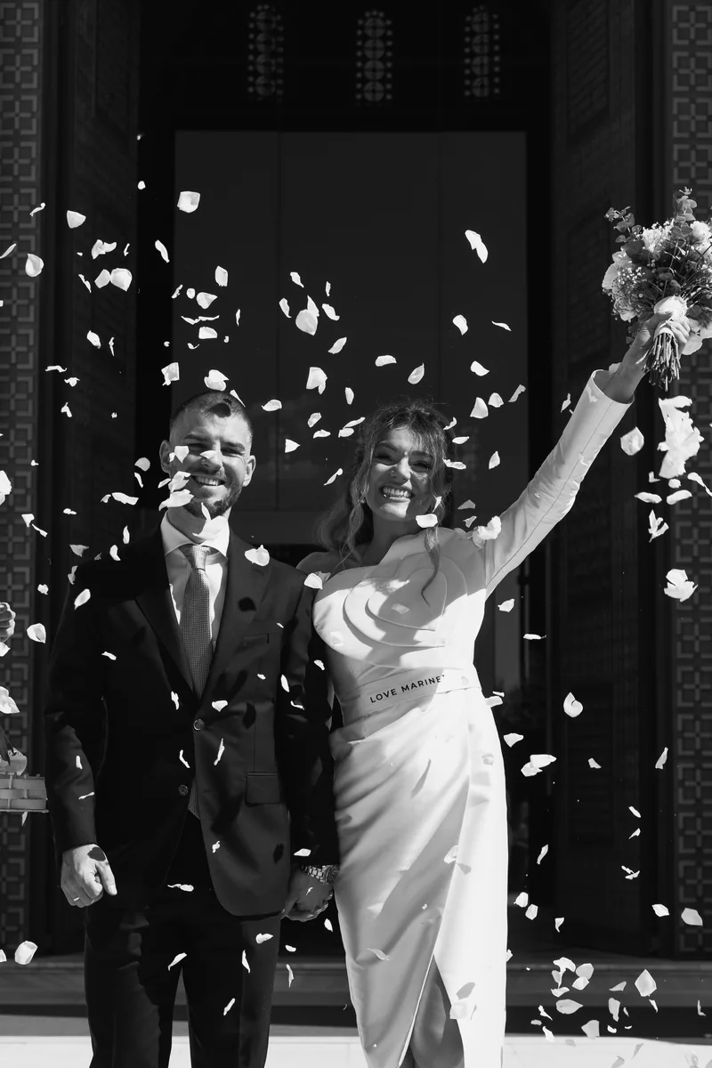 Newlyweds laugh amid a shower of white petals just outside the church doors.