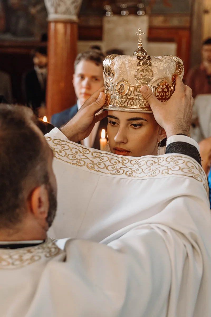 A priest holds a golden ceremonial crown above the bride's head during an Orthodox wedding ceremony.