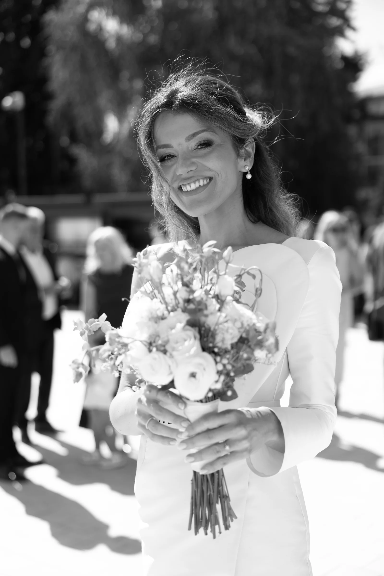 Radiant bride holds her bouquet outdoors with windswept hair and a bright smile.