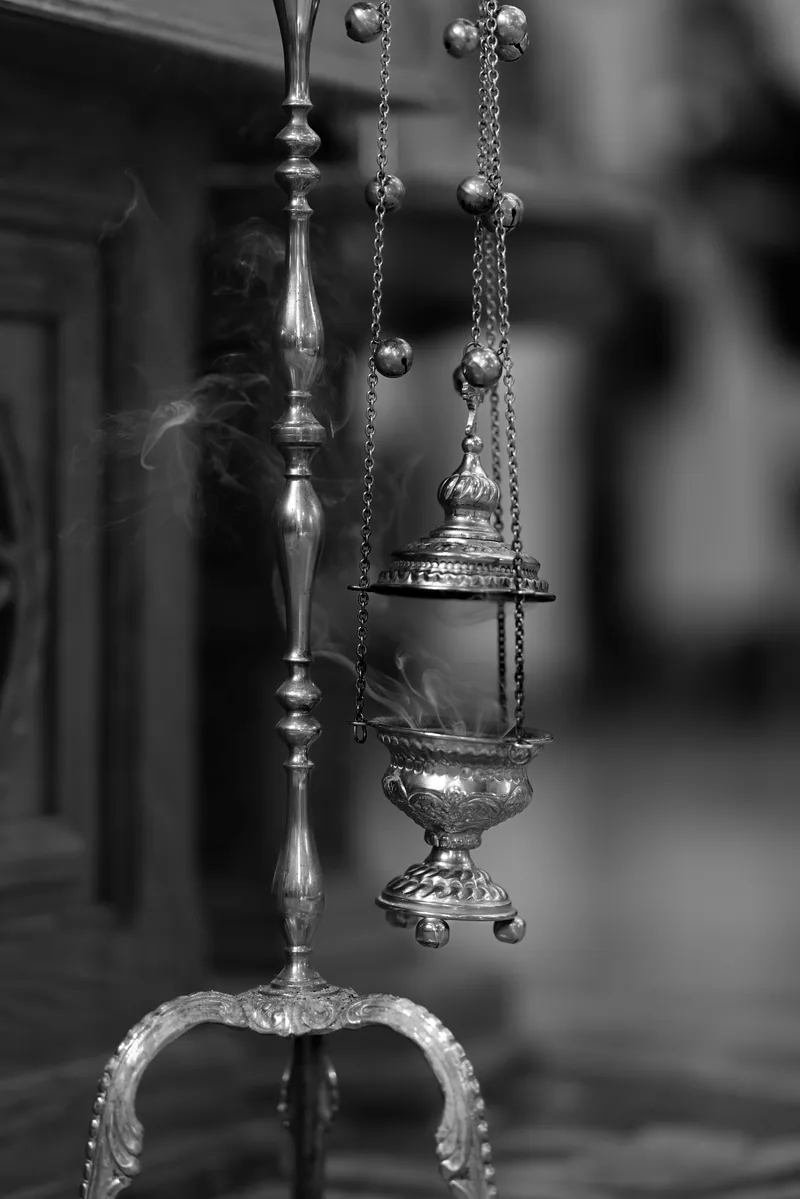 Black and white silver church censer on chains with incense smoke rising beside a tall stand