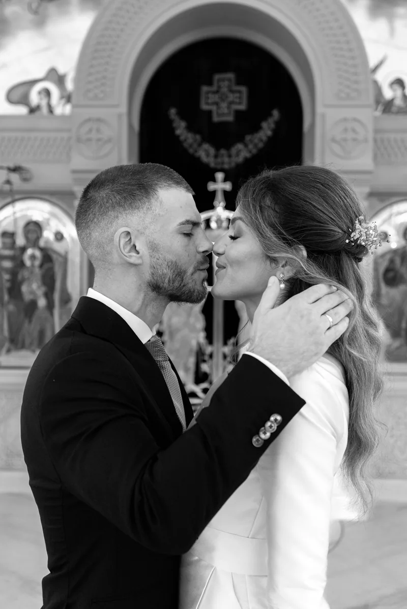 Close black and white portrait of a couple about to kiss in front of golden church icons.