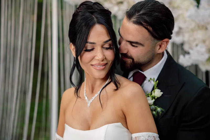 Color portrait of a groom nuzzling a smiling bride who wears a sparkling diamond necklace