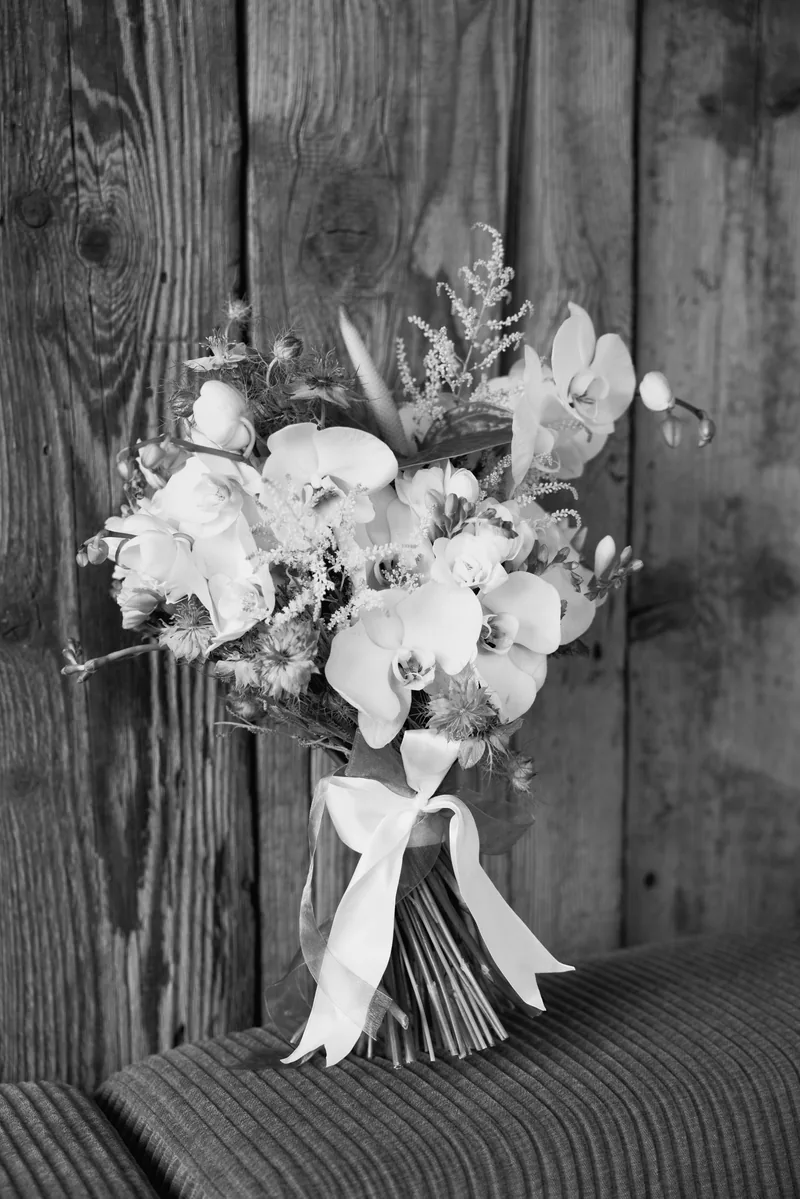 Black and white bridal bouquet of white orchids and dried stems tied with ribbon against wood