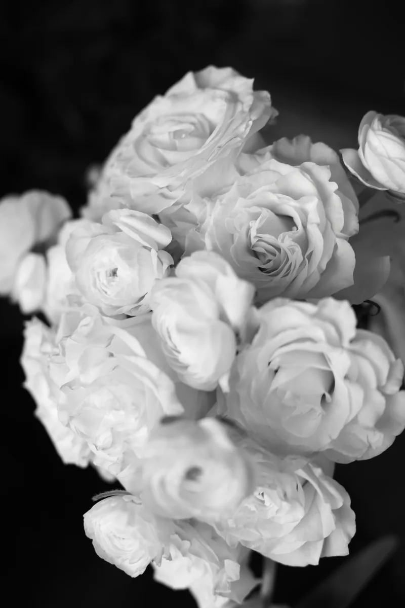 A black and white close-up of a lush bridal bouquet of white roses and ranunculus.