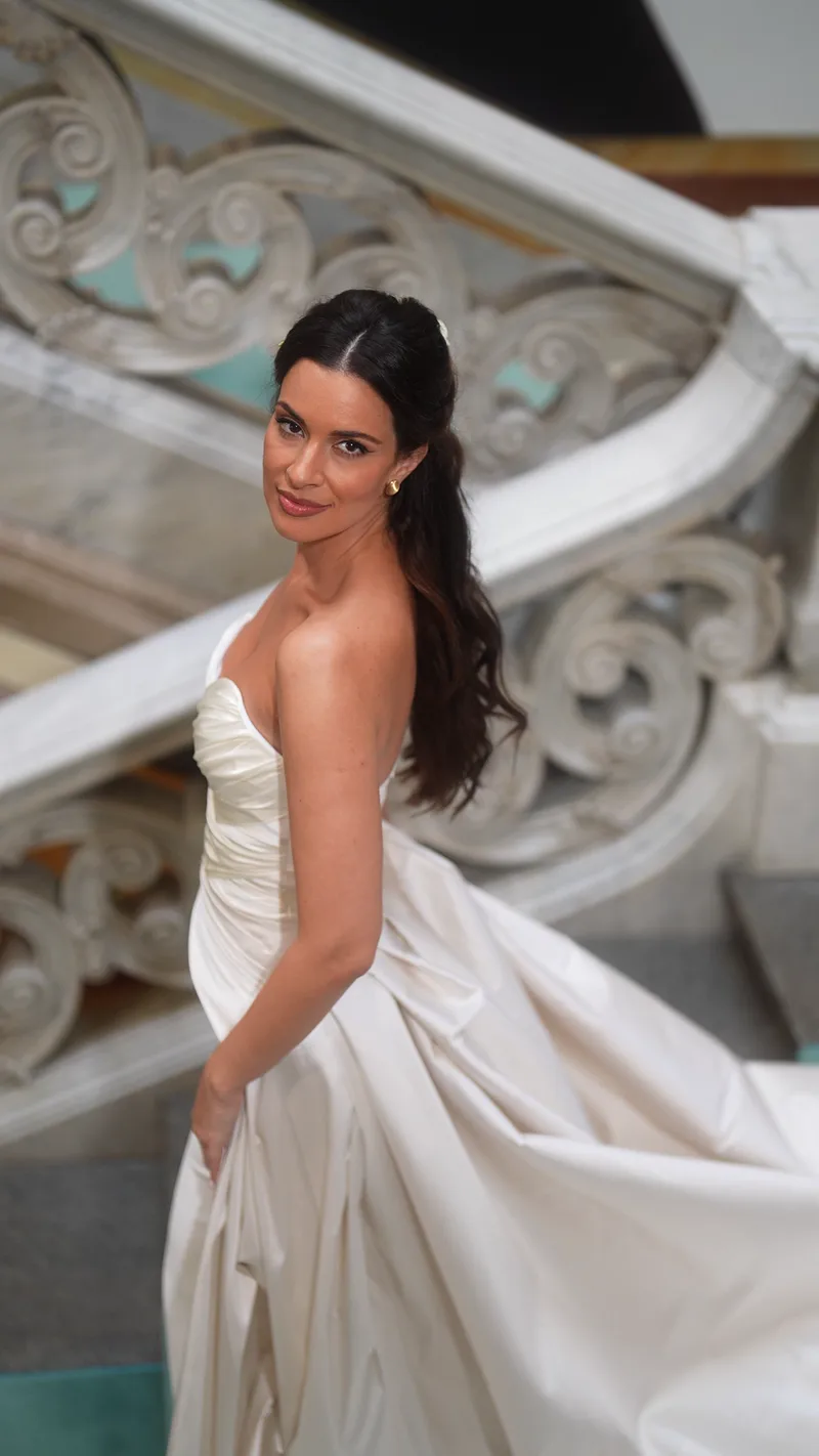A bride in a satin gown looks back over her shoulder on a sweeping marble staircase.